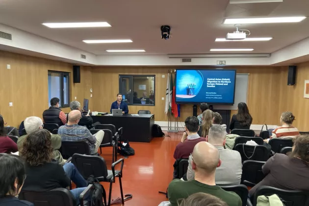 a room with people, big screen and the presenter SHerzod Eraliev at a conference